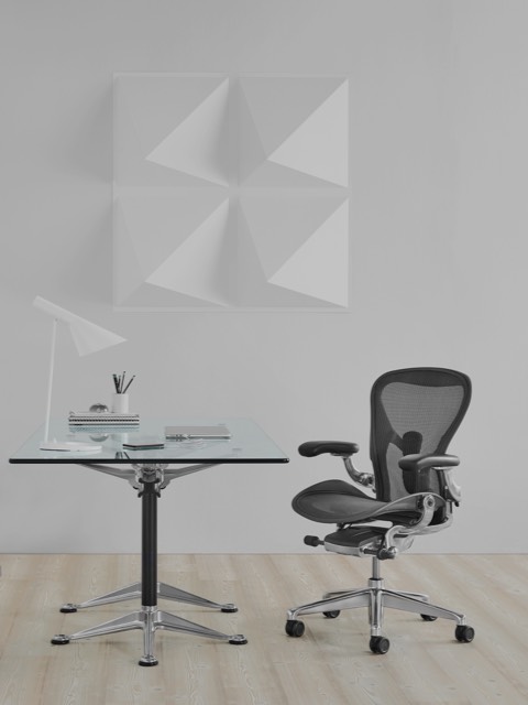 Uma mesa Burdick quadrada com tampo em vidro, usada como escrivaninha e complementada com uma cadeira de escritório Aeron preta. Uma mesa Burdick quadrada com tampo em vidro, usada como escrivaninha e complementada com uma cadeira de escritório Aeron preta.