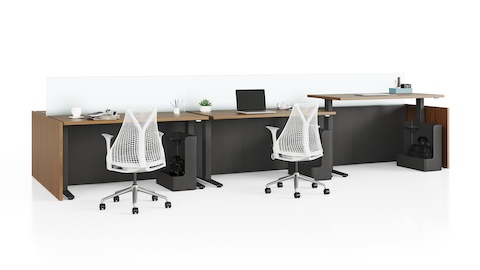 Estaciones de trabajo Canvas Channel con mesas de altura ajustable en madera oscura, pantallas de vidrio, y sillas para oficinas Sayl blancas.
