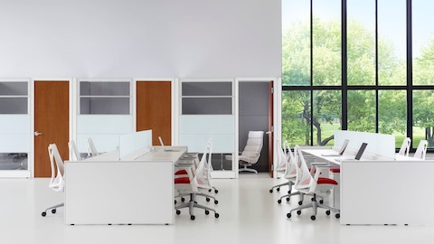 Espacio de trabajo abierto con grandes ventanas al aire libre, bancas Ethospace y sillas de oficina Sayl blancas con asientos tapizados en rojo.