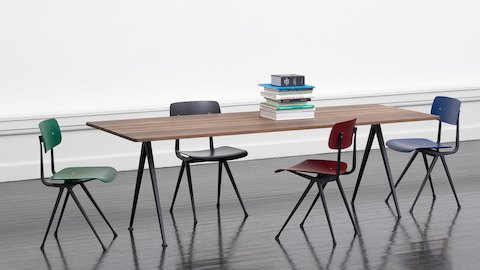 Sillas Result en verde, negro, rojo y azul con estructura en negro, ubicadas en torno a una mesa Pyramid en roble ahumado.