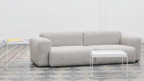 Mesa de café Tray en blanco y una mesa auxiliar Tray dispuestas junto a un sofá seccional Mags Soft en gris.