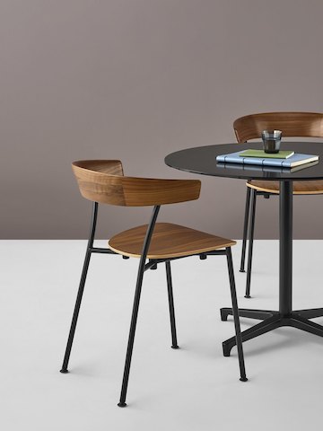 Dos Sillas Leeway con bases metálicas en negro y asientos y respaldos de madera oscura, alrededor de una mesa Saiba negra donde se apoyan una taza de café y computadoras portátiles.