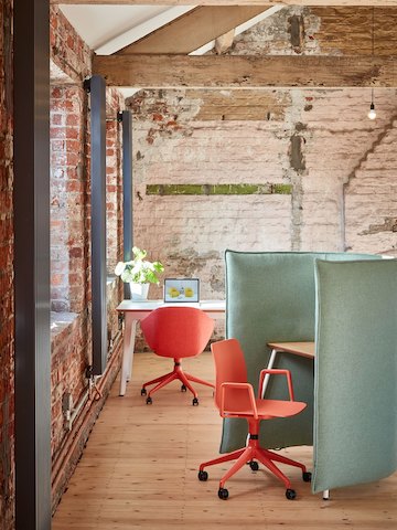An orange Polly Chair with orange powder coated 5-star base stationed at a pale green Cloud 1.5 Desk. An orange Always Chair is in the background.