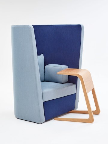 Una silla Busby de NaughtOne, tapizada en azul y celeste, vista desde un ángulo junto a una mesa Riley de roble. 