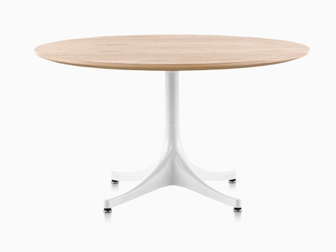 Una mesa de pedestal Nelson redonda con una parte superior de madera clara y base blanca.