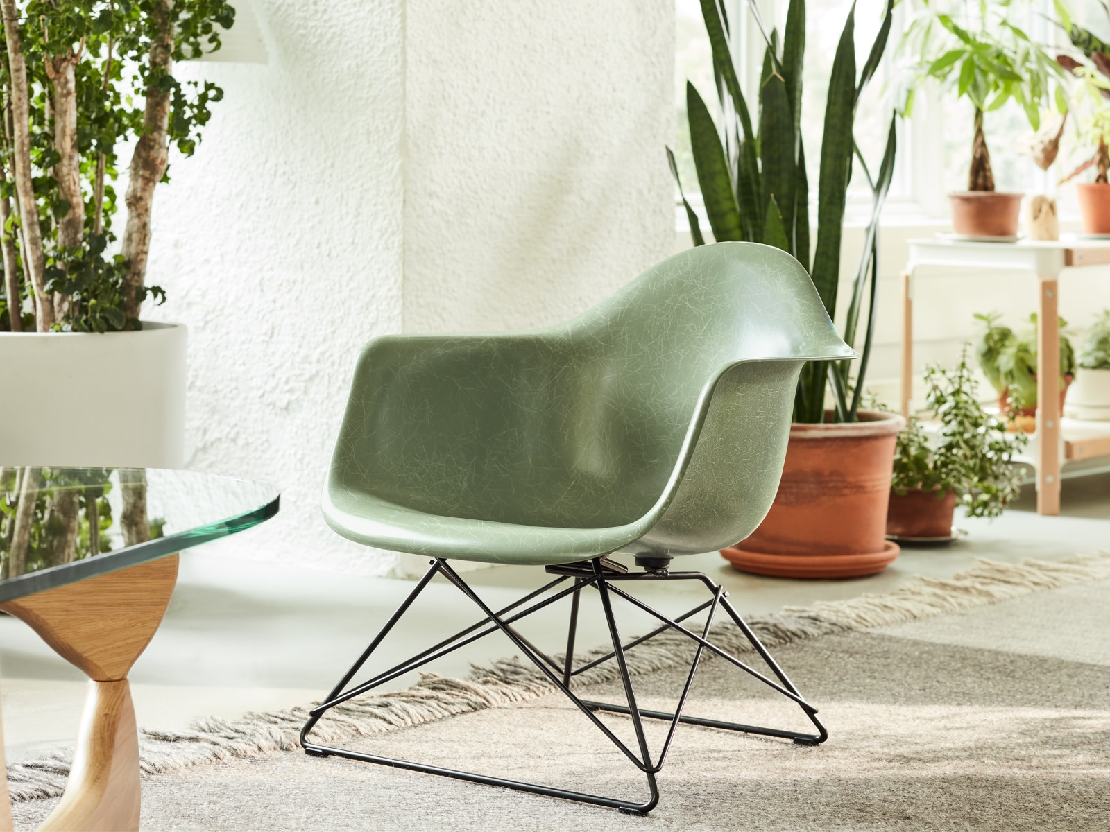 Una vista en primer plano de la poltrona de fibra de vidrio moldeada Eames con una base de alambre baja en un ambiente de estar casual al lado de una mesa Noguchi.